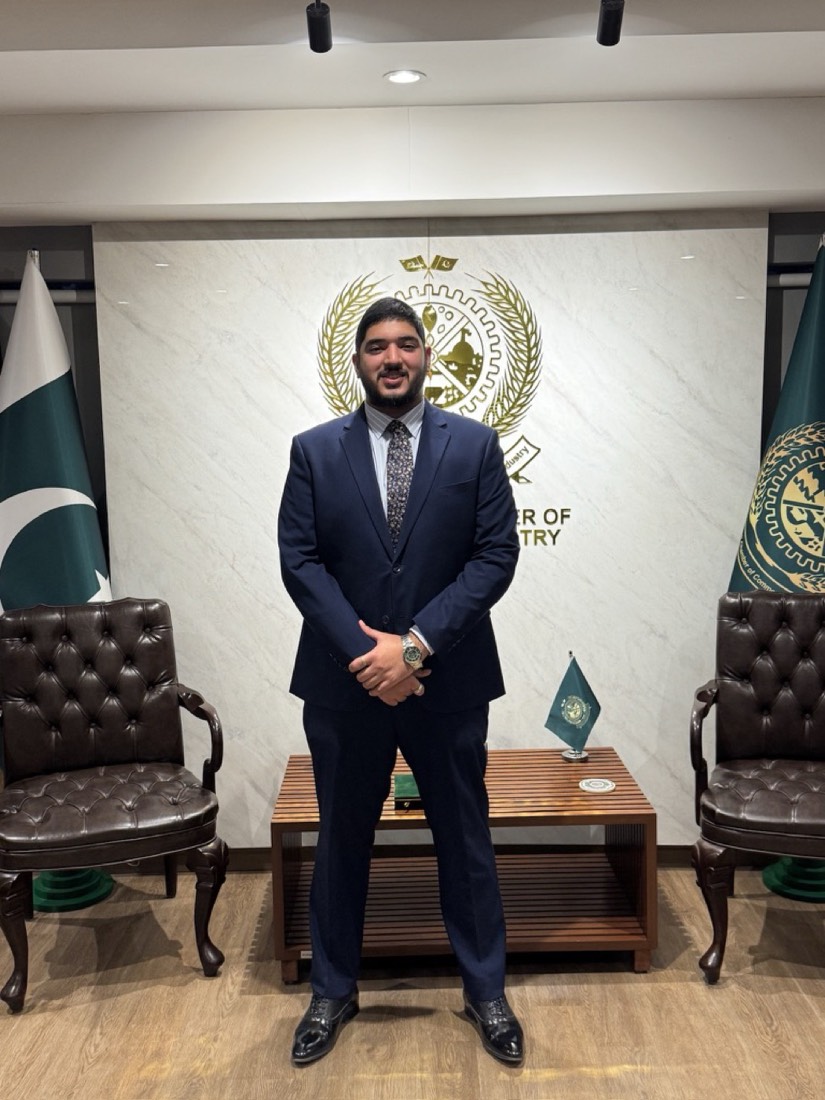 Husnain in a suit at a chamber of commerce office with Pakistan flags