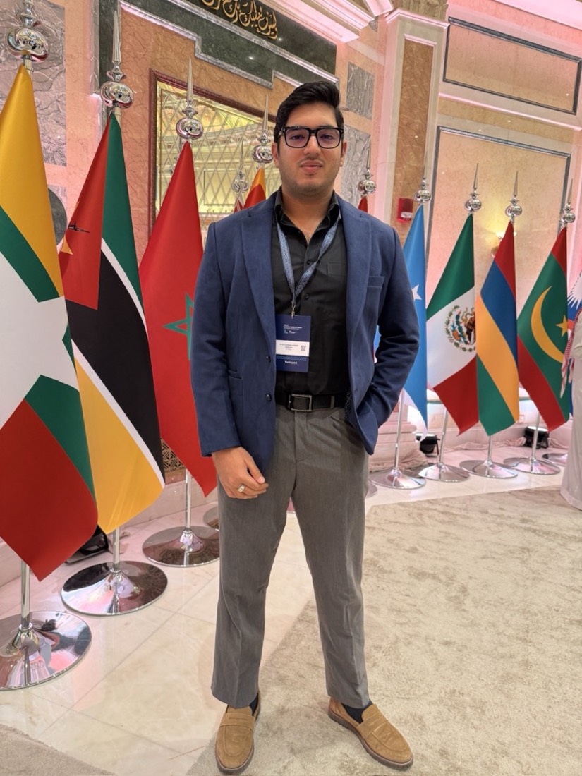 Husnain with a participant badge beside international flags