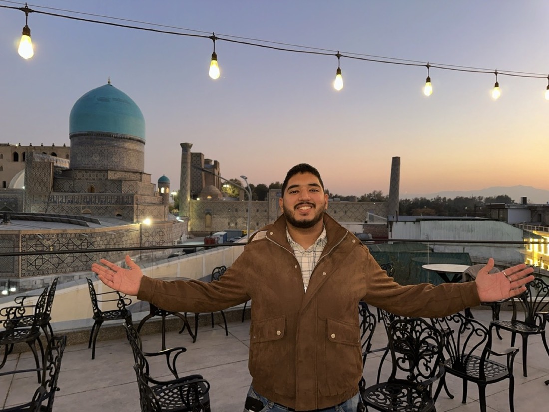 Husnain on a rooftop with a blue-domed historic building behind him at dusk