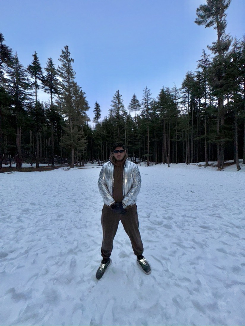 Husnain in a silver jacket in a snowy pine forest