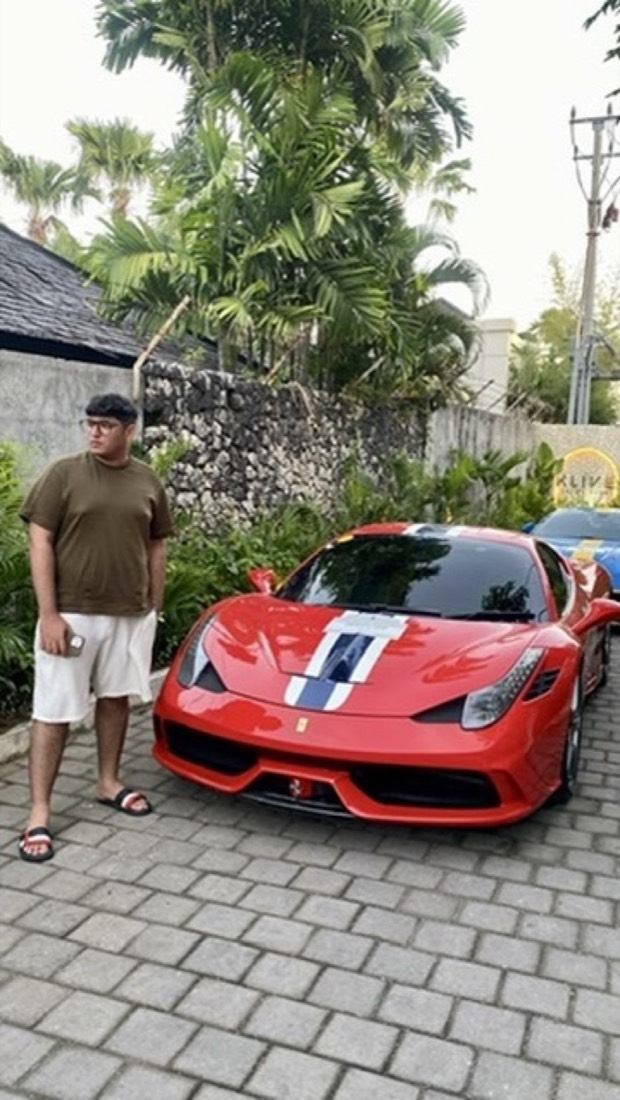 Husnain beside a red sports car on a tropical street