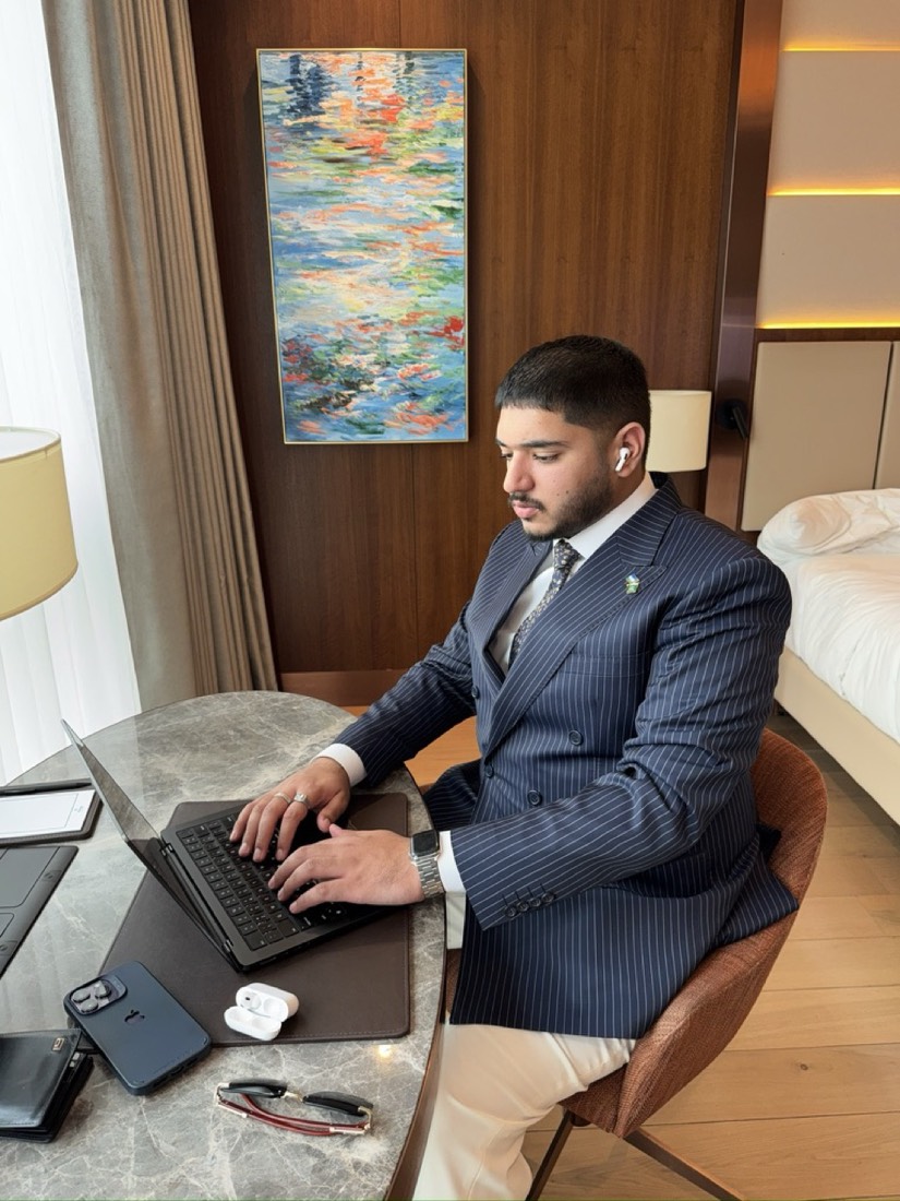 Husnain working on a laptop at a hotel desk in a pinstripe suit
